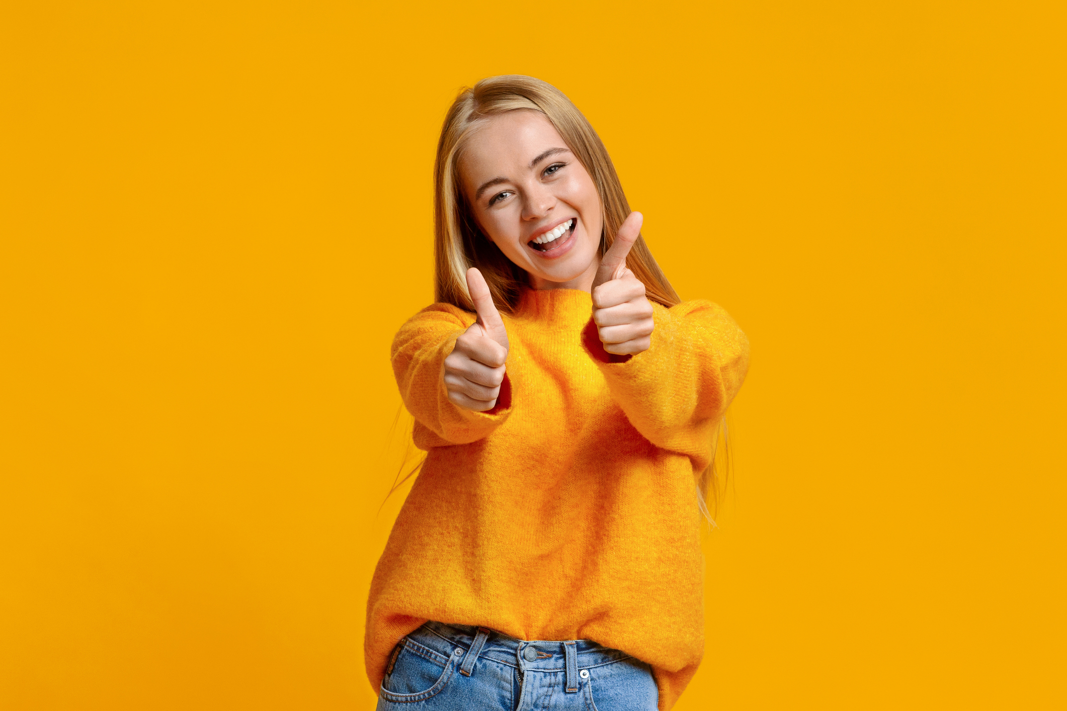 Choosing the Best HVAC Company in Bullhead City, AZ. Portrait of a joyful girl showing thumbs up and smiling at the camera, against an orange background.