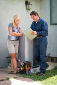 Air conditioner repairman in uniform and a clipboard discussing, HVAC System Analysis.